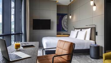Habitación de hotel moderna con una cama, un escritorio con una computadora portátil, una silla y un televisor en la pared.