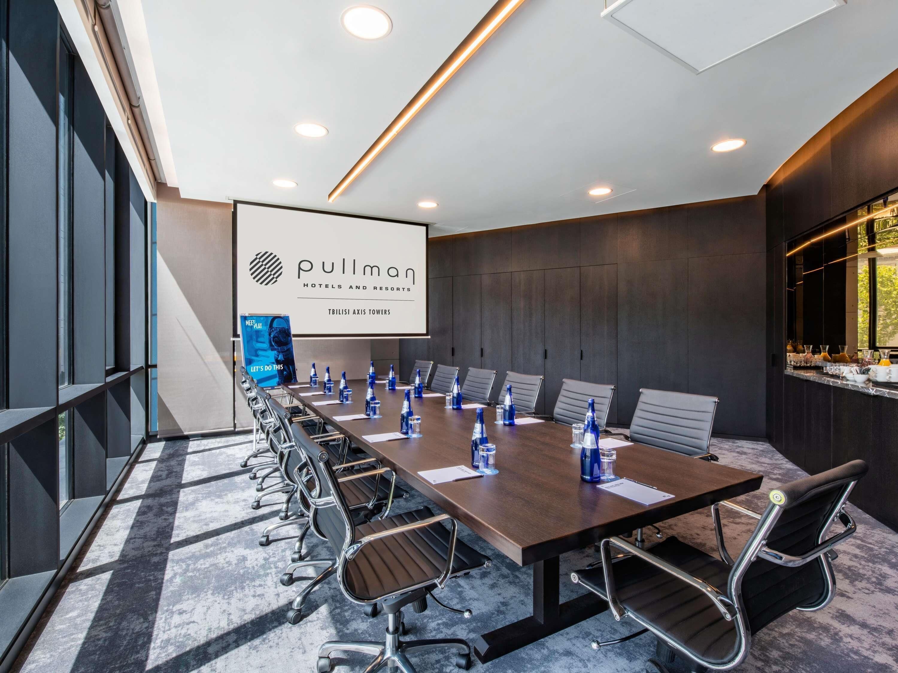 A modern conference room with a long table, chairs, and a screen displaying 'Pullman Hotels and Resorts'.