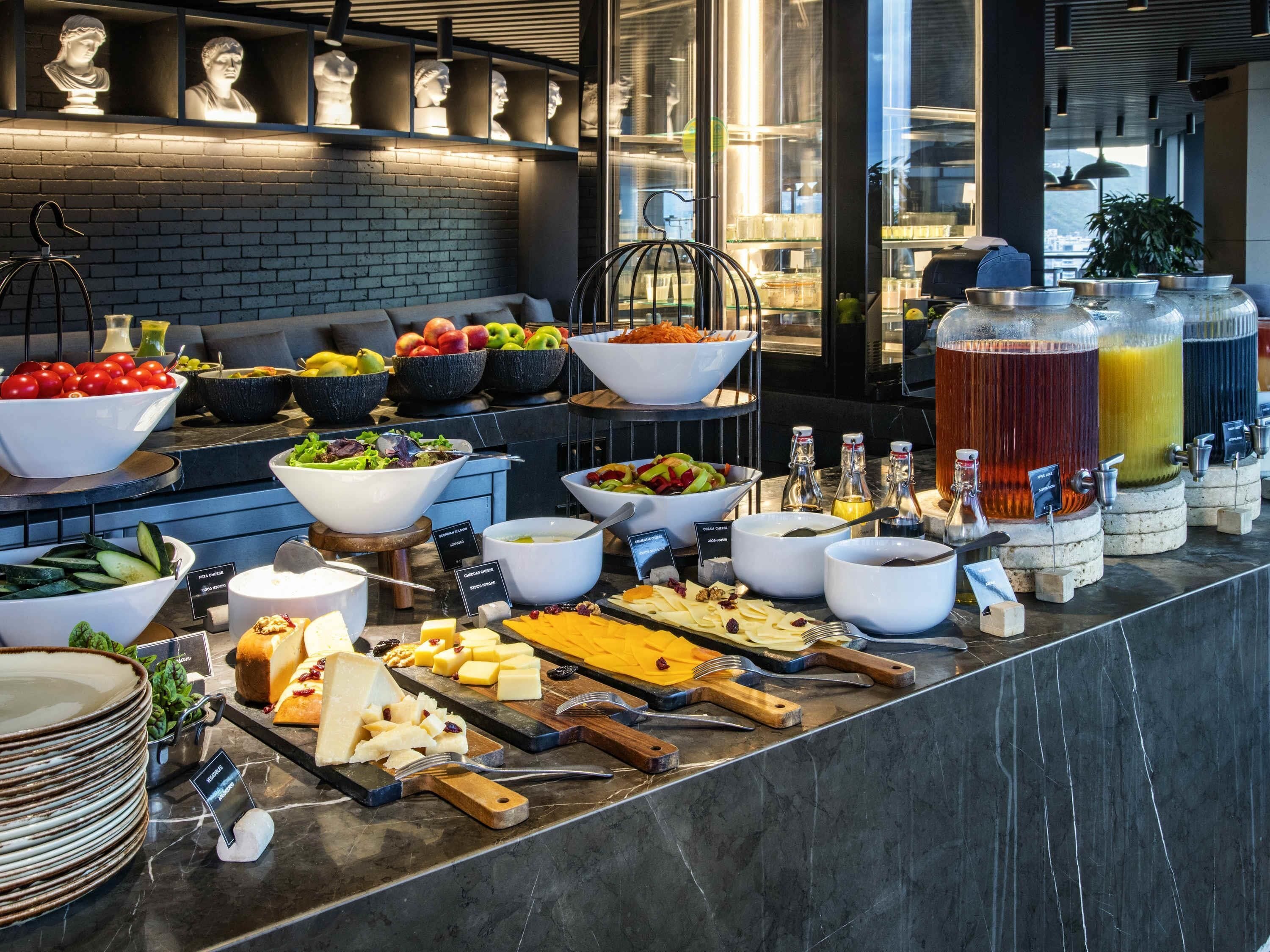 A buffet with various food items and beverages, including fruits, salads, cheeses, and drinks.