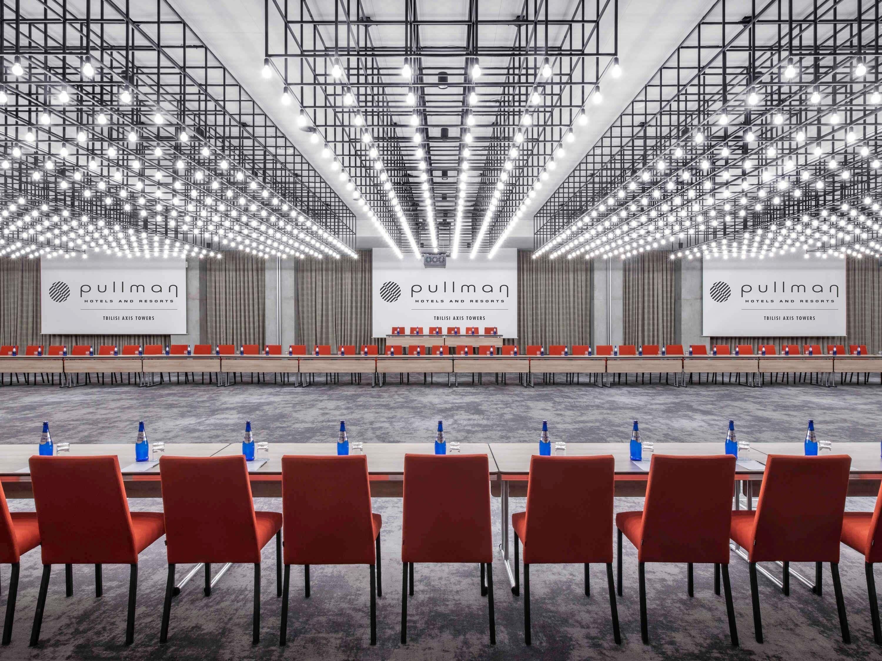 A conference room with a long table, red chairs, and a banner reading 'Pullman Hotels and Resorts'.