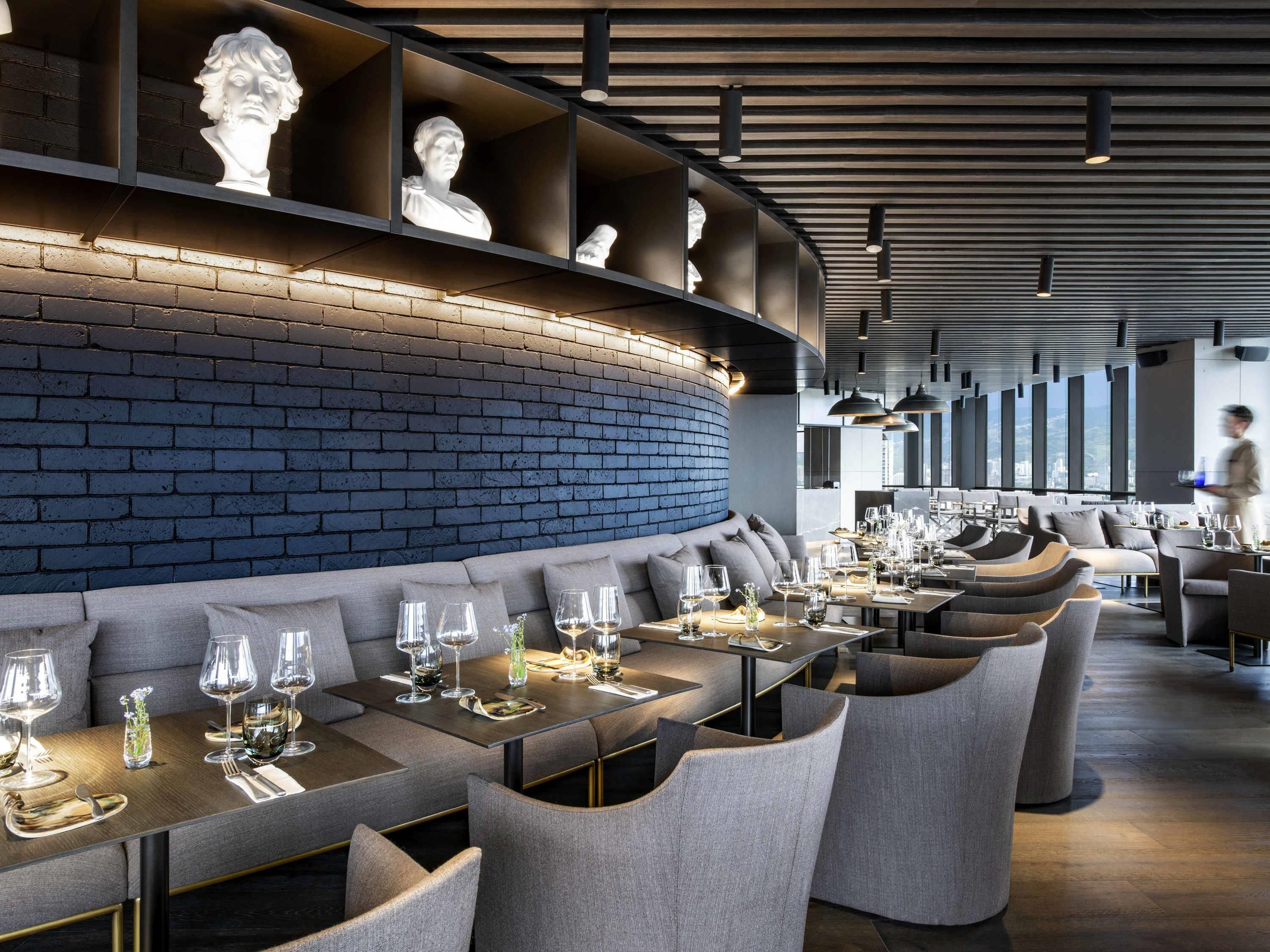 A modern restaurant with a brick wall, recessed seating, and a view of the city.