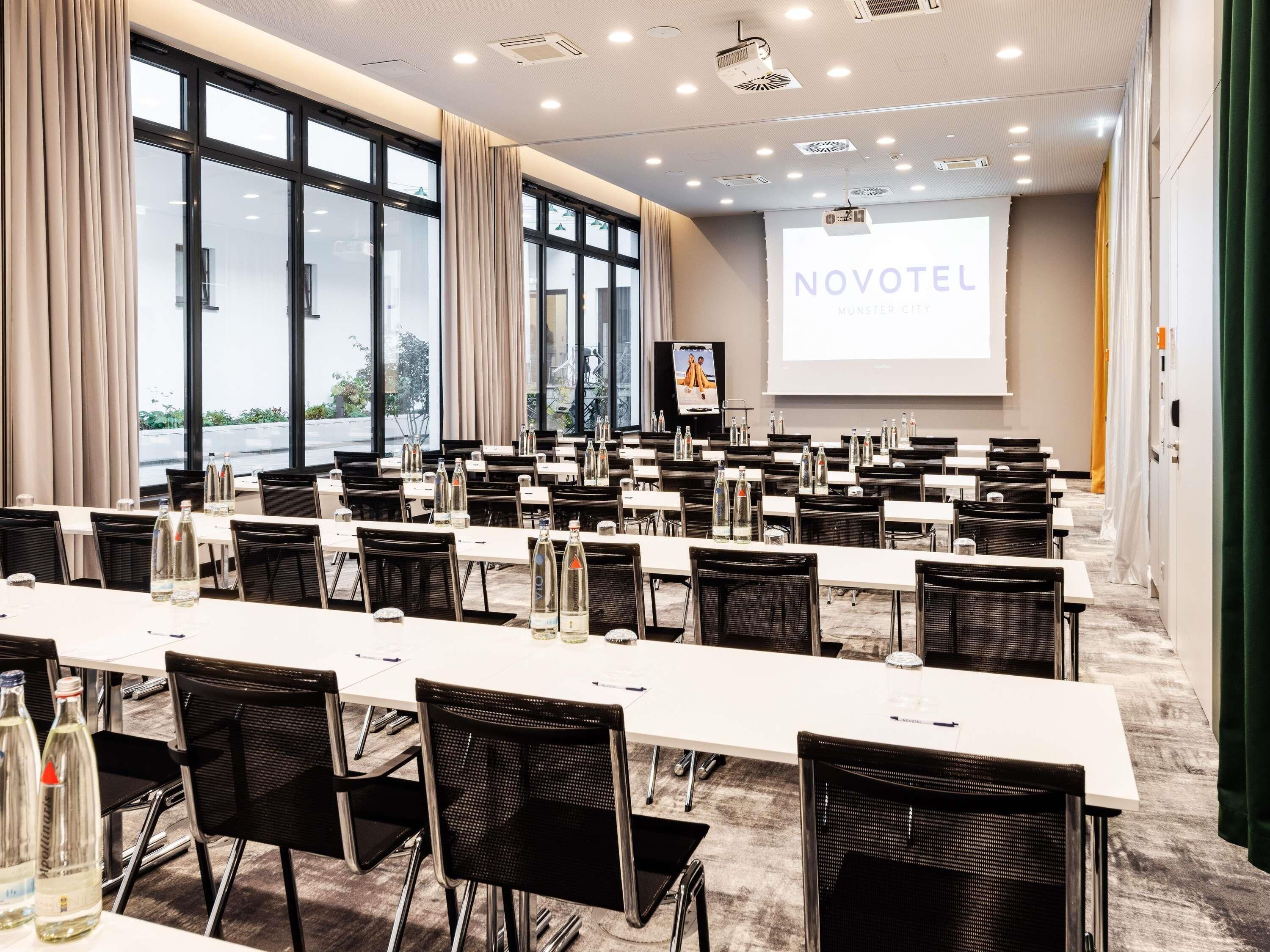 A conference room with tables, chairs, and a projection screen displaying 'NOVOTEL.'
