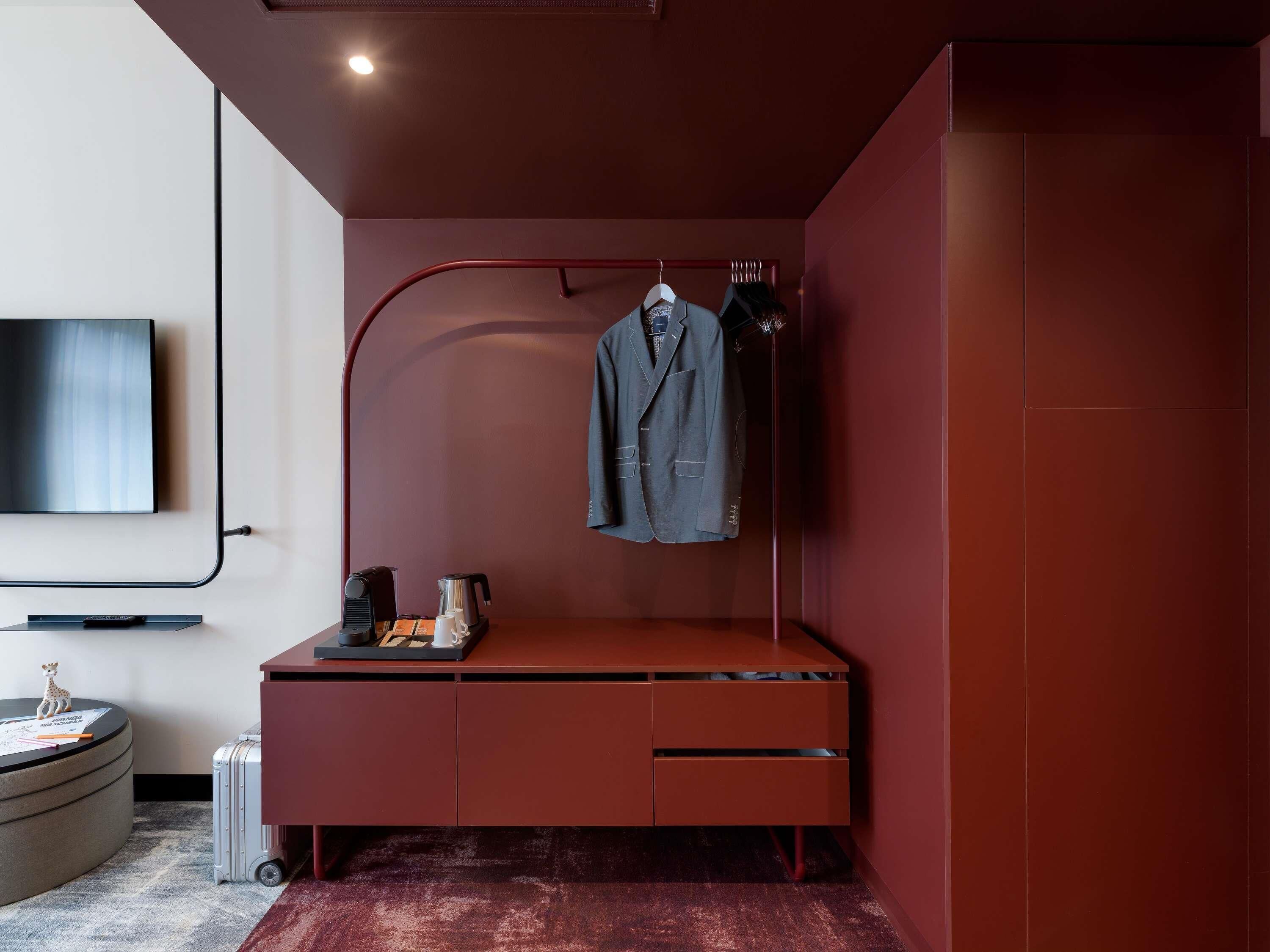 Una habitación moderna con escritorio, perchero, televisor y maleta.