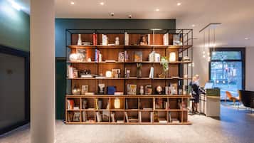 Una moderna zona de recepción con una amplia estantería de madera llena de libros y objetos decorativos, un mostrador de recepción y vistas a la calle a través de un gran ventanal.