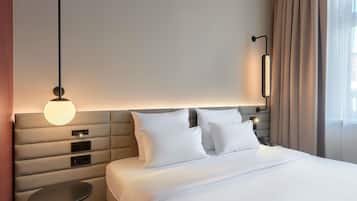 Ein Hotelzimmer mit einem großen Bett, einem runden Tisch, einer Wandlampe und einem Fenster mit Vorhängen.