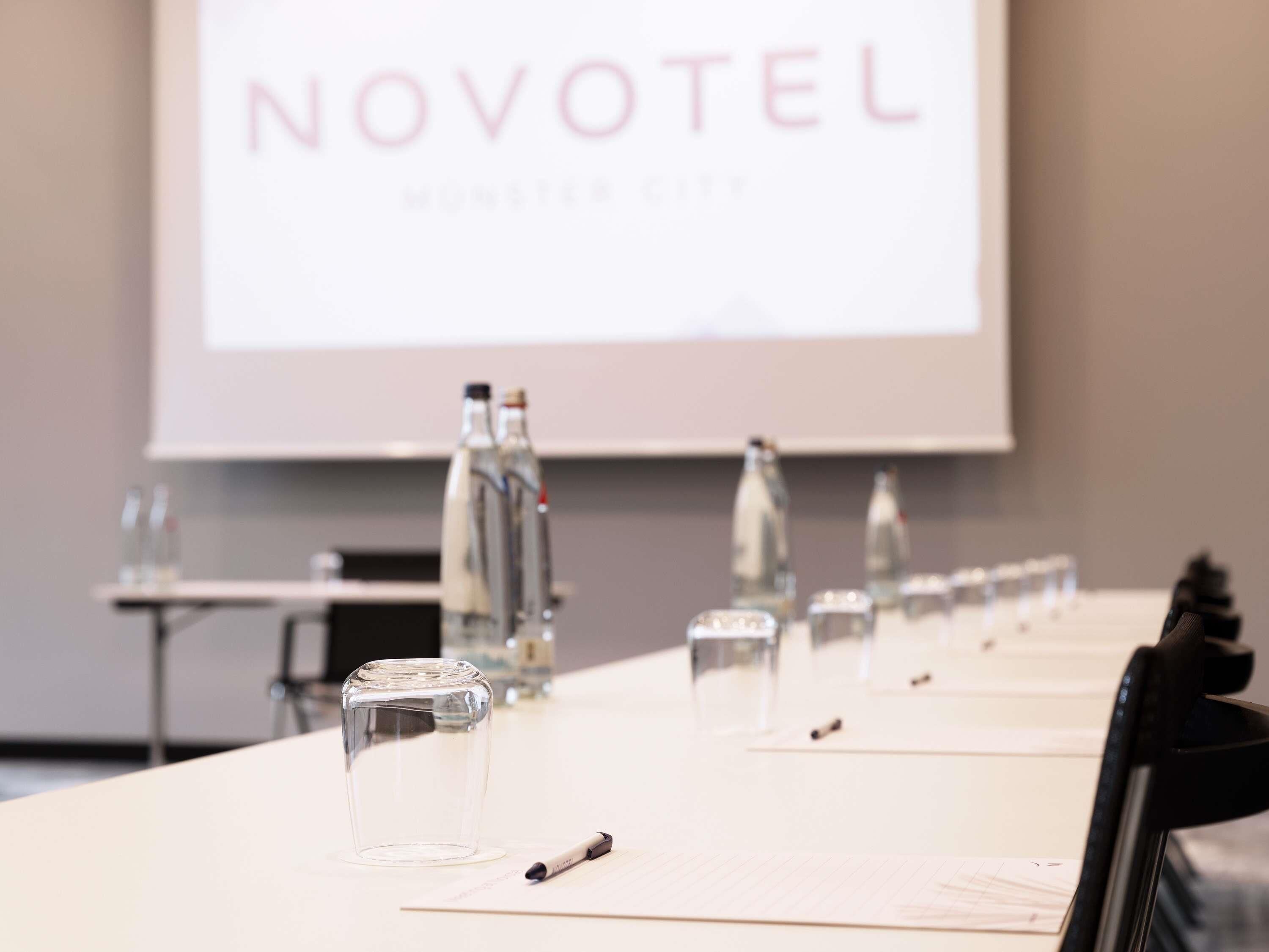 A conference table with water bottles, a pen, and a projector screen displaying 'NOVOTEL'.