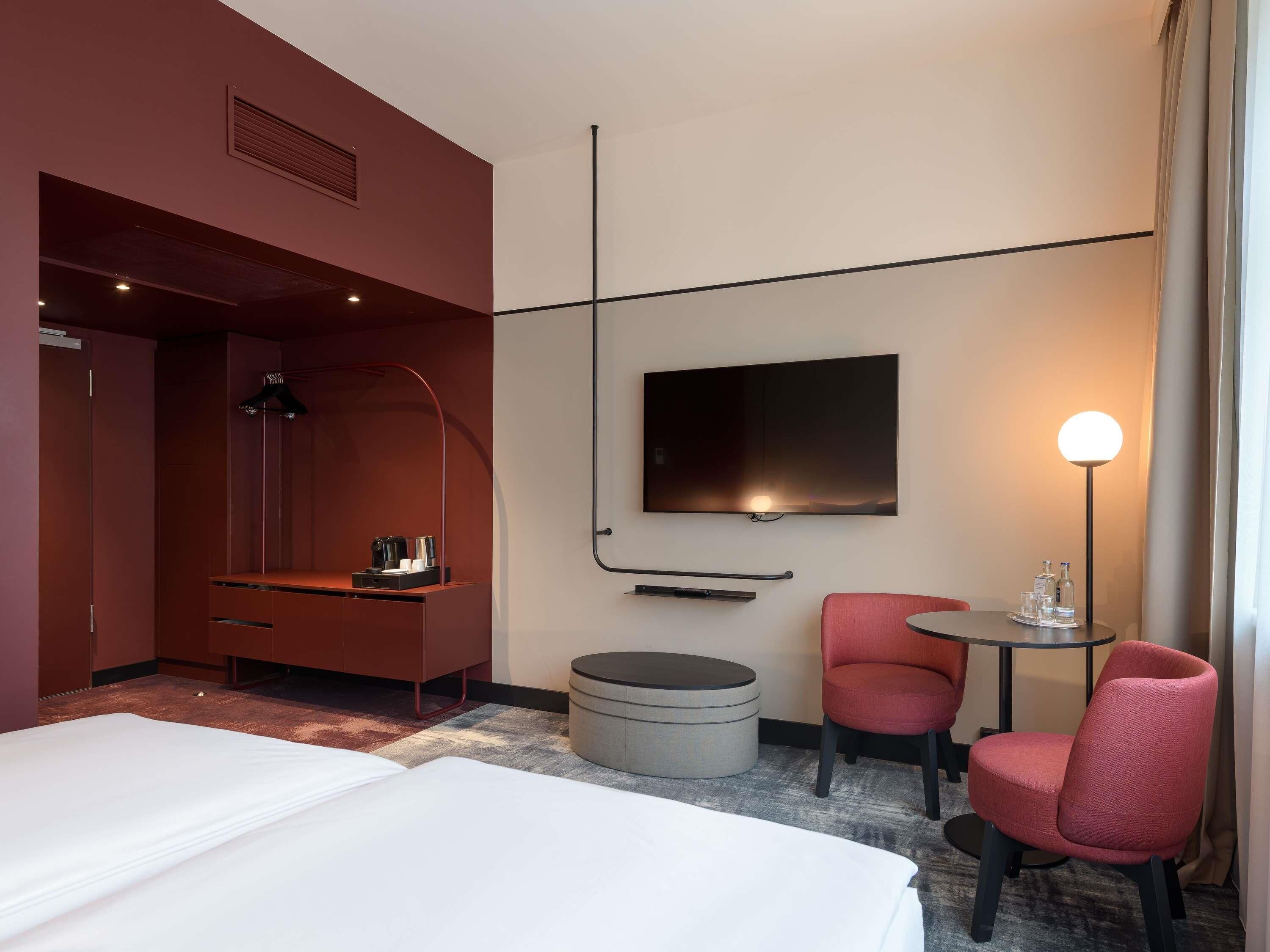Habitación de hotel con cama, televisión, escritorio con lámpara, una silla y una mesita con botellas.