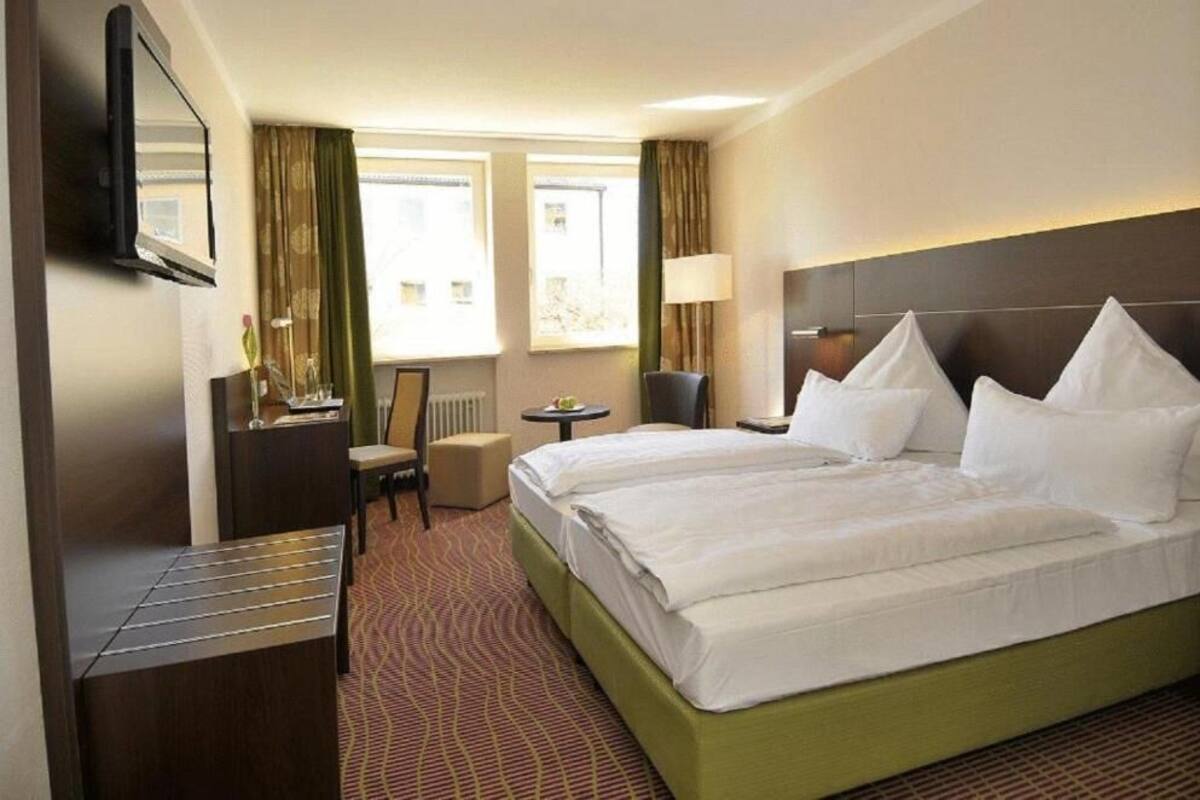 Habitación de hotel con dos camas, un escritorio, una silla, un televisor y una ventana con cortinas.