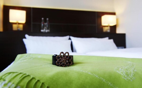 A hotel room with a neatly made bed, a green bedspread, and two wall-mounted lamps. - Stern Hotel Soller (Ismaning)
