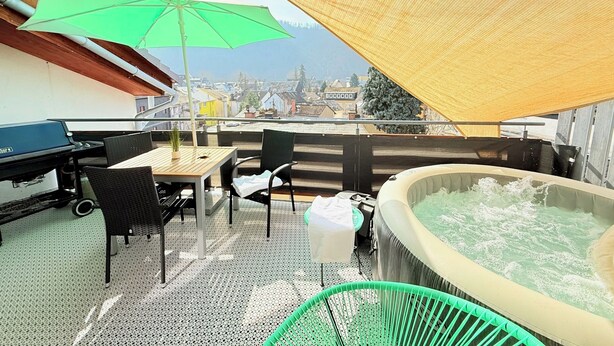 Tagterrasse med jacuzzi, udendørs møbler og udsigt over byen.