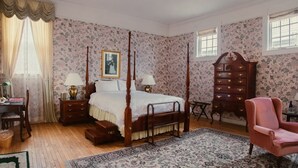 A bedroom with a four-poster bed, a dresser, a chair, and a desk with a lamp. - Victorian Mansion Jim-Dandy Suite (Bennington)