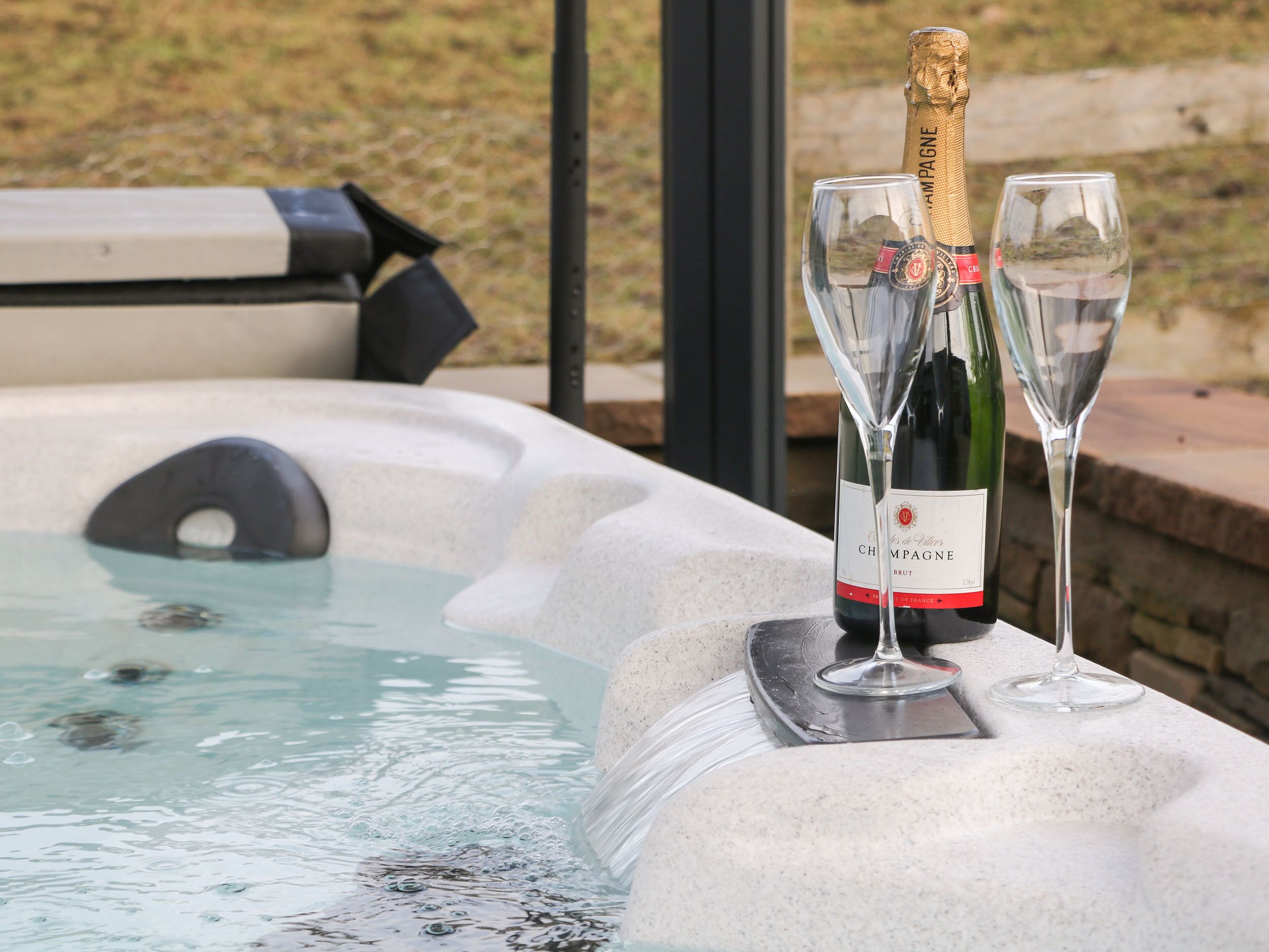 A hot tub with two champagne bottles and glasses.
