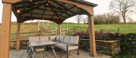 An outdoor patio with a wooden pergola, a cushioned seating area, and a stone table.