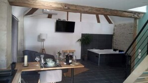 Ein Essbereich mit einem Holztisch, gedeckt für zwei Personen, einem an der Wand montierten Fernseher und einer Küchenzeile mit Spüle und Arbeitsfläche.