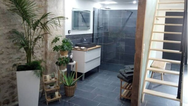 Ein modernes Badezimmer mit Dusche, Waschbecken und Spiegel. Üchtöpfe und eine Holzleiter sind ebenfalls vorhanden.