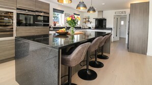 Cozinha moderna com ilha central, banquetas, iluminação pendente e armários de madeira.