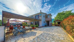 A two-story house with a stone-paved patio, outdoor seating area, and a covered section with umbrellas. - Six Bedroom Villa with Pool (Kaštel Stari)