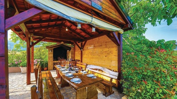 An outdoor wooden pavilion with a dining table set for four, benches, and a bench with a cushioned seat. - Six Bedroom Villa with Pool (Kaštel Stari)