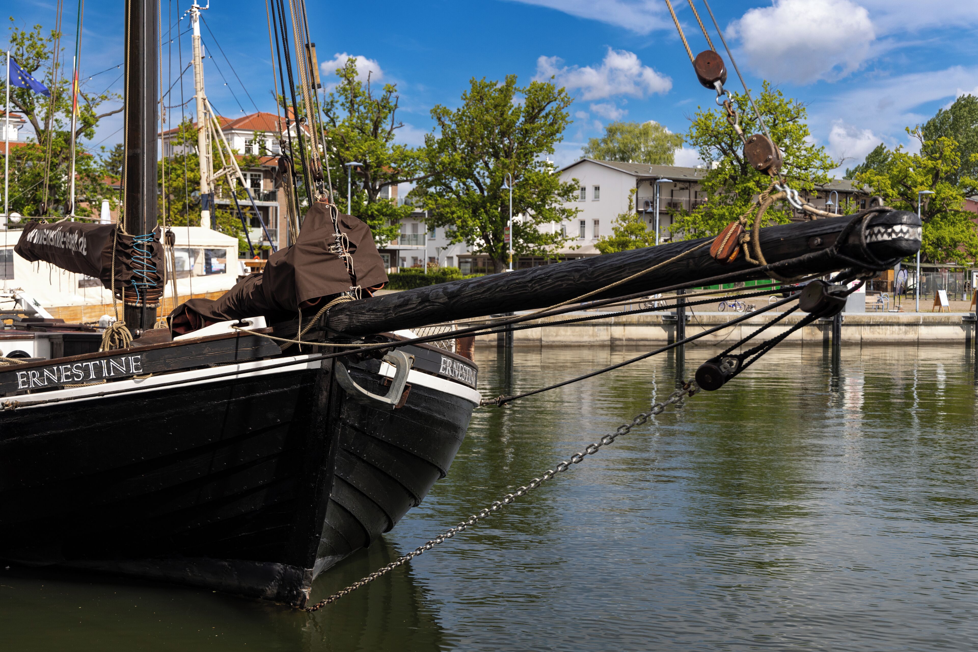 Un bote negro llamado 'ERNESTINE' atracado en un puerto deportivo con un amarre de cadena.