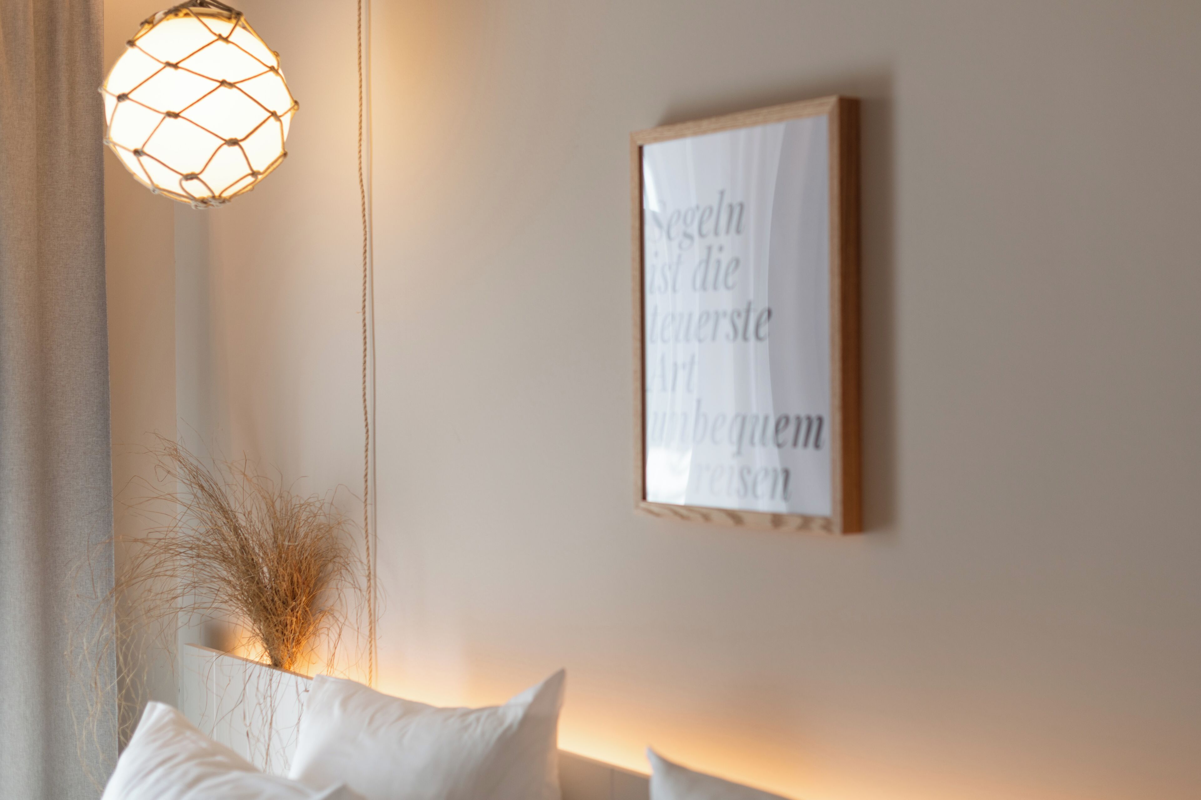 Una habitación con una lámpara fijada a la pared, un texto enmarcado en la pared y un cojín blanco.