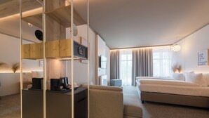 A modern hotel room with a sofa, a small table, a TV, and a large window with curtains. - Hafenhotel zu Putbus (Putbus)