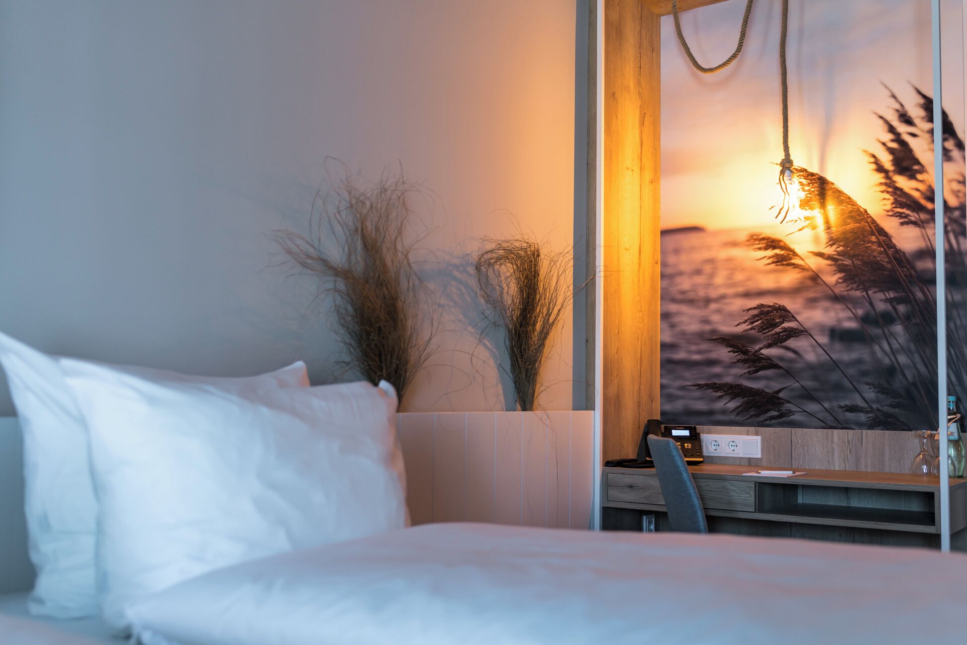 A hotel room with a bed, a desk, and a wall-mounted TV displaying a sunset view.