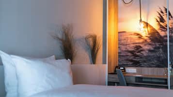 A hotel room with a bed, a desk, and a wall-mounted TV displaying a sunset view.