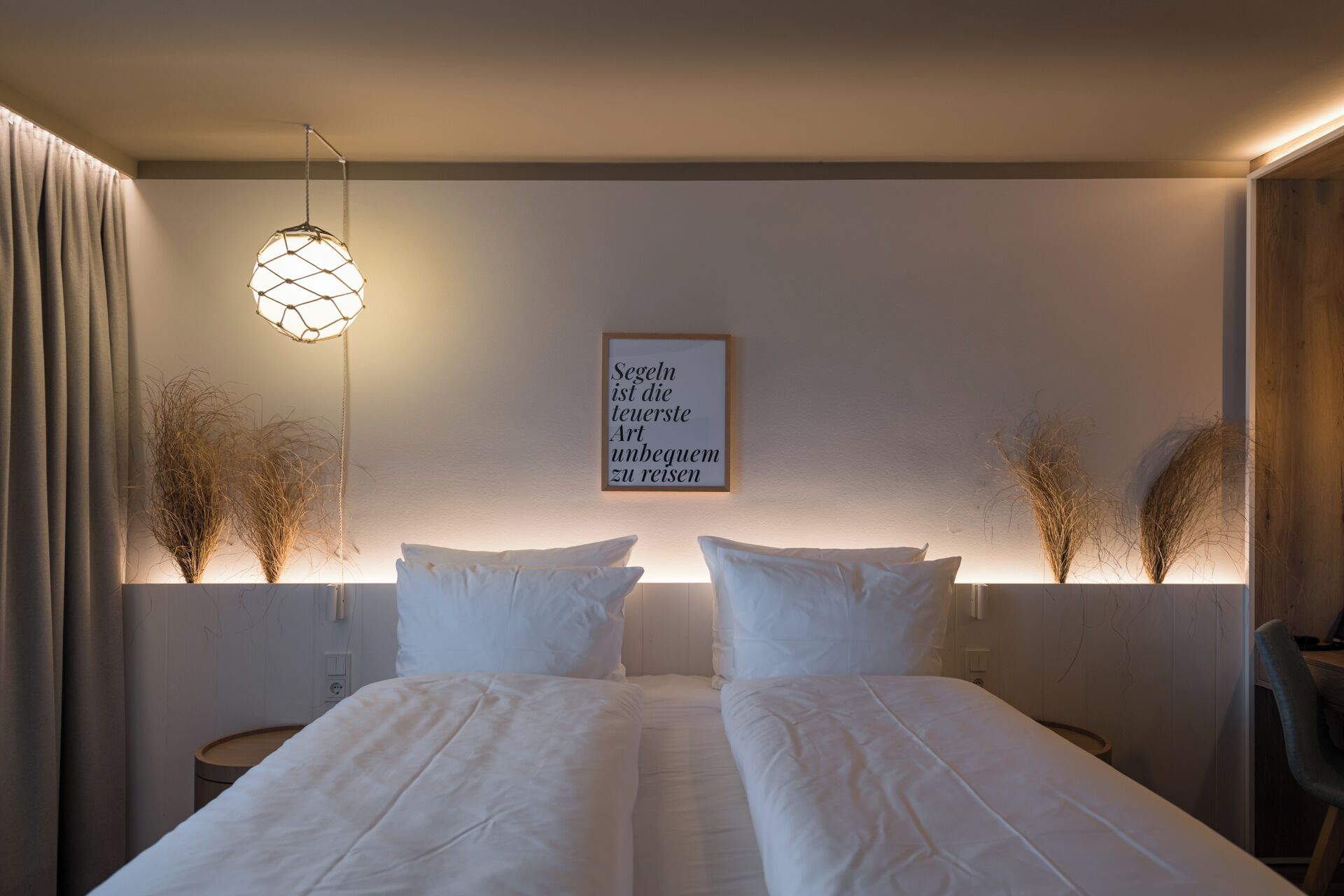 A hotel room with a bed, a wall-mounted light fixture, and a framed quote on the wall.