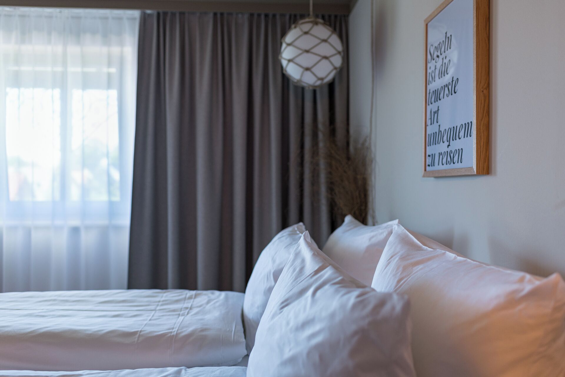 Une chambre à coucher avec un lit, des rideaux, un luminaire suspendu et une citation encadrée accrochée au mur.