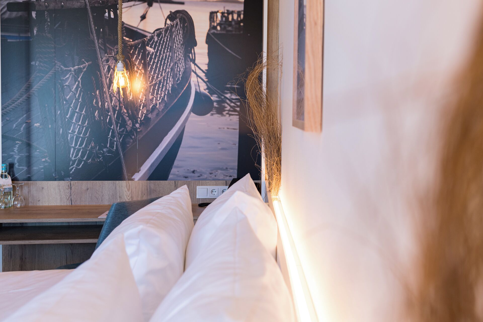 Una cama con ropa blanca, cabecera de madera y televisor de pared mostrando una escena náutica.