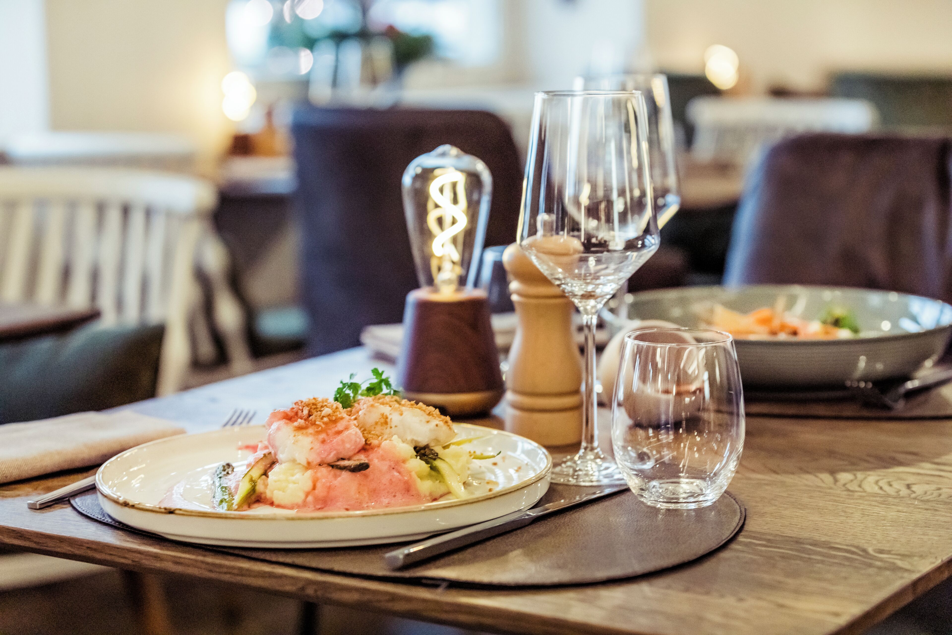 A dining table with plates of food, wine glasses, and a salt and pepper set.
