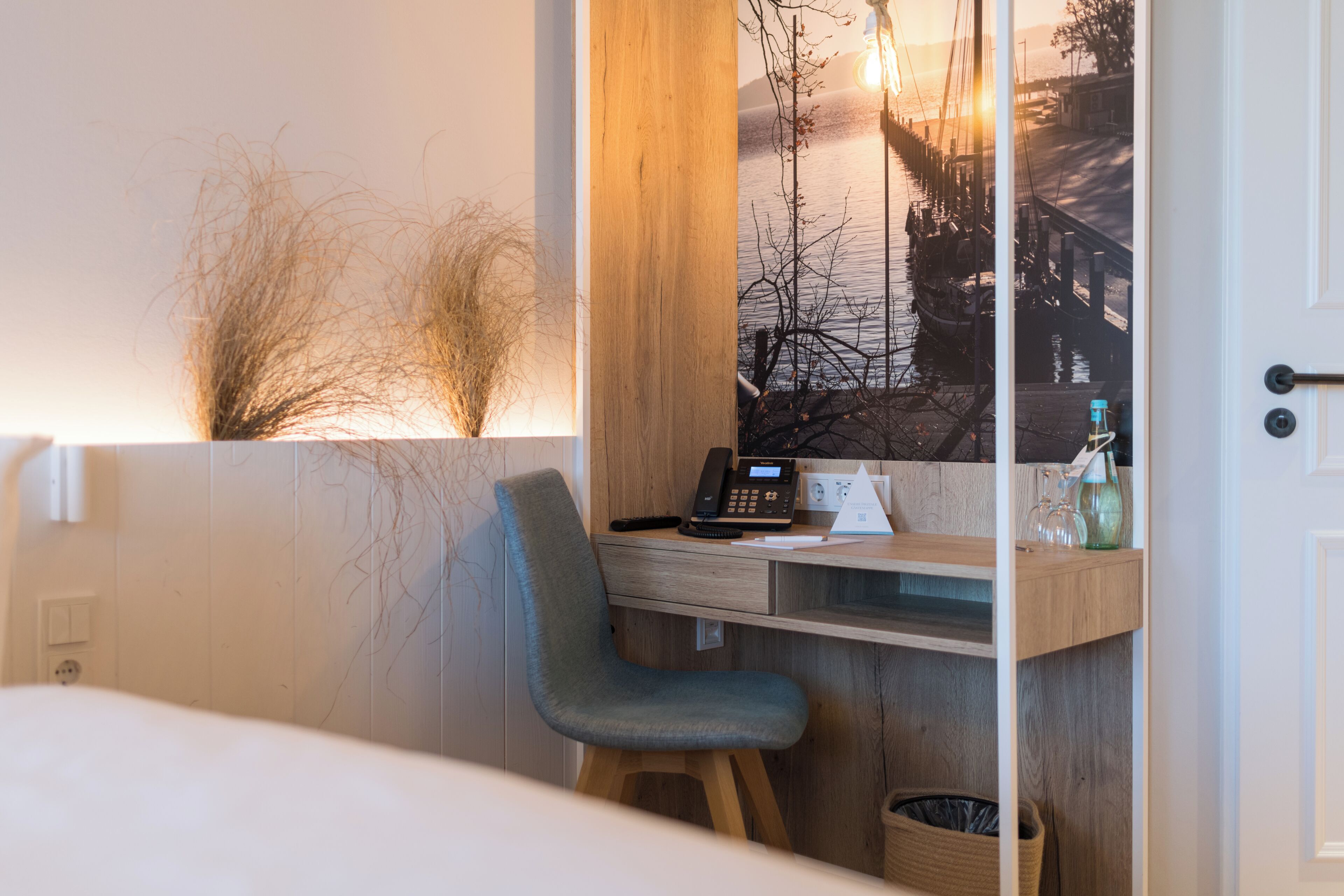 Habitació d'hotel moderna amb escriptori de fusta, una cadira, un telèfon i vista d'un moll i embarcacions.