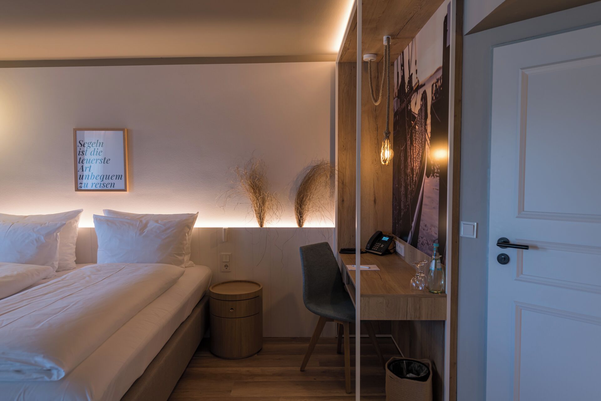 A bedroom with a bed, bedside table, lamp, and a wall-mounted artwork.
