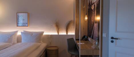 A bedroom with a bed, bedside table, lamp, and a wall-mounted artwork.