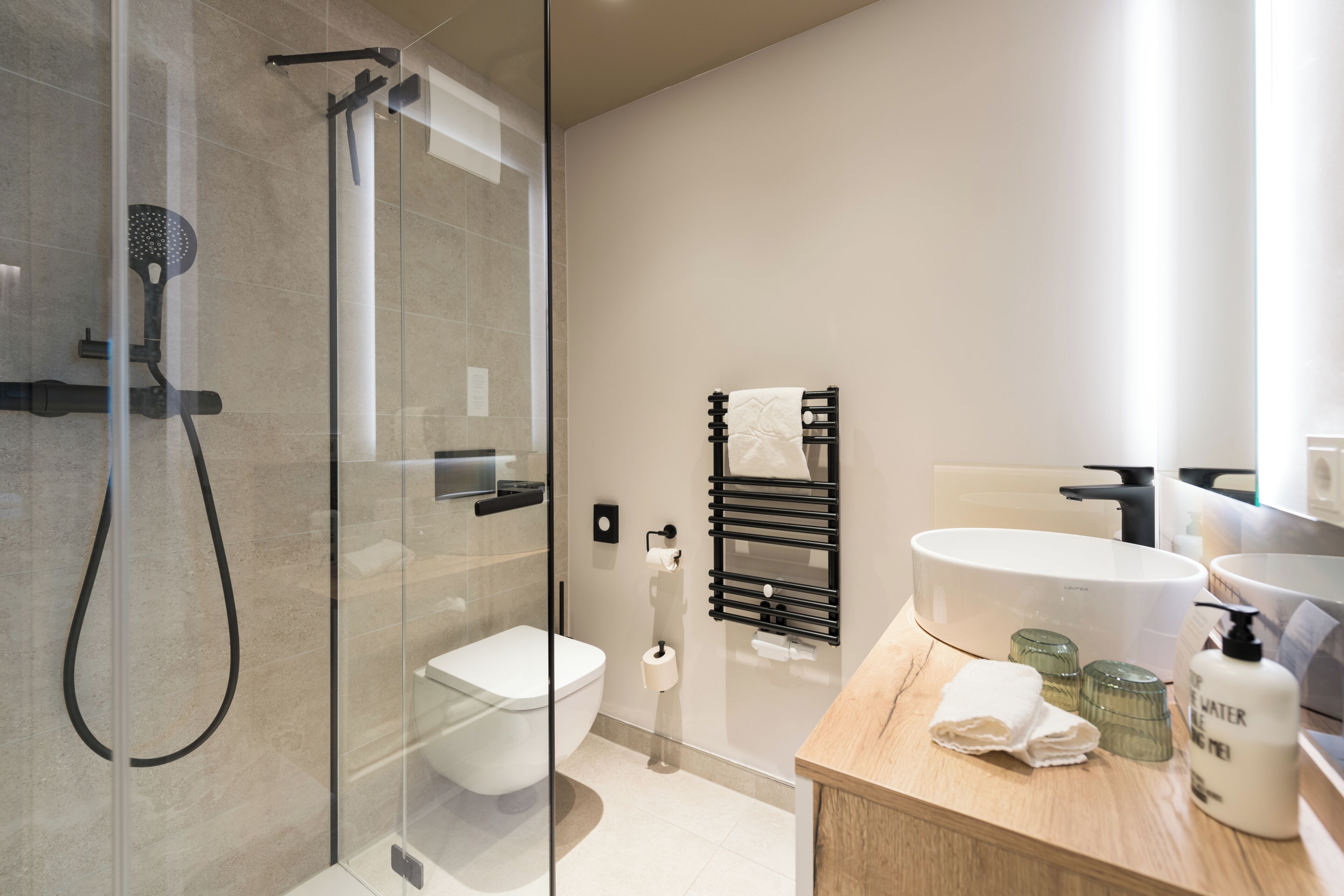 A modern bathroom with a glass-enclosed shower, a toilet, a sink, and a towel rack.