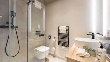 Un baño moderno con ducha envuelta en vidrio, inodoro, lavamanos y toallero.