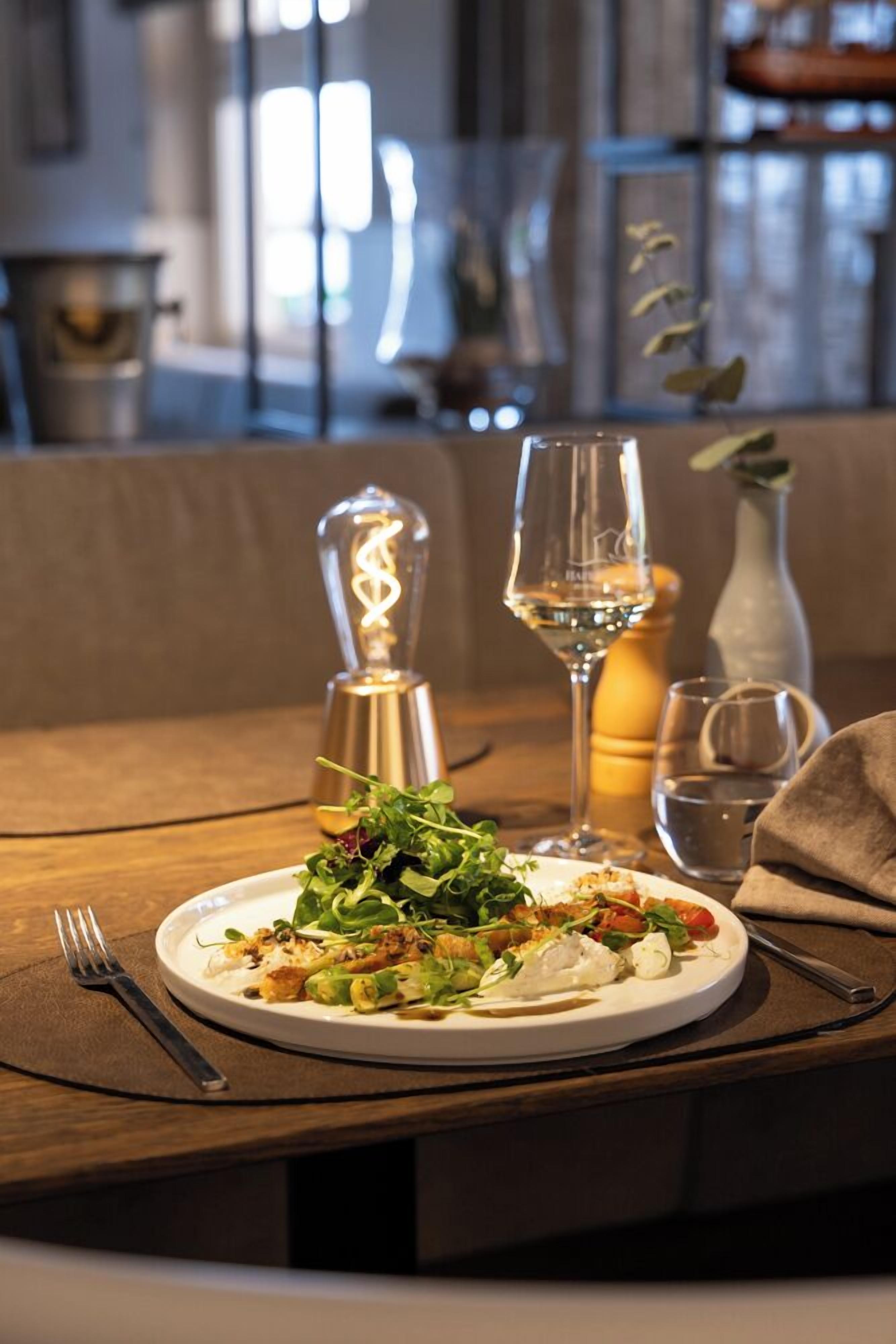 A dining table with a plate of food, a wine glass, a salt shaker, and a candle.