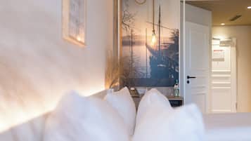 Una cama con ropa de cama blanca, un cuadro en la pared y una puerta que da a otra habitación.