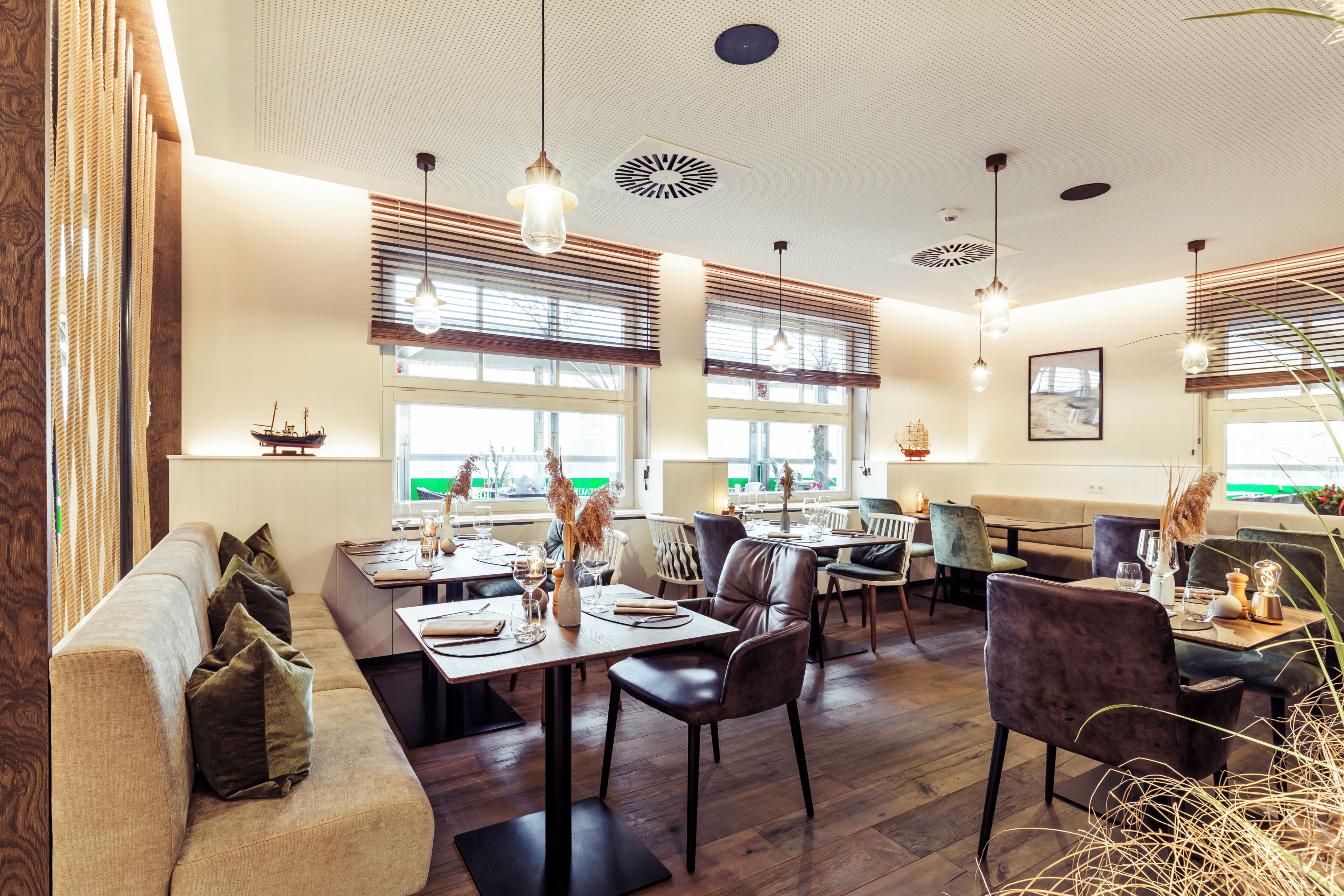Interior de restaurante con suelo de madera, mesas, sillas e iluminación colgante.