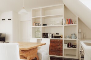 A modern kitchen with white cabinetry, a wooden table, and various kitchen appliances.