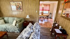 Un salon comprenant un canapé, un fauteuil, une table avec une lampe, et un coin repas avec une table et des chaises.