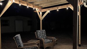 An outdoor covered patio with string lights, two wicker chairs, and a table.