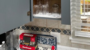 A kitchen with grey cabinets, a window with blinds, and a countertop with a box of Kwikset keys.
