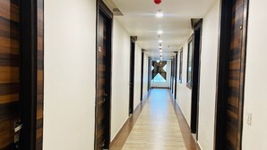 Un long couloir étroit, avec des portes en bois de chaque côté et un sol recouvert de moquette.