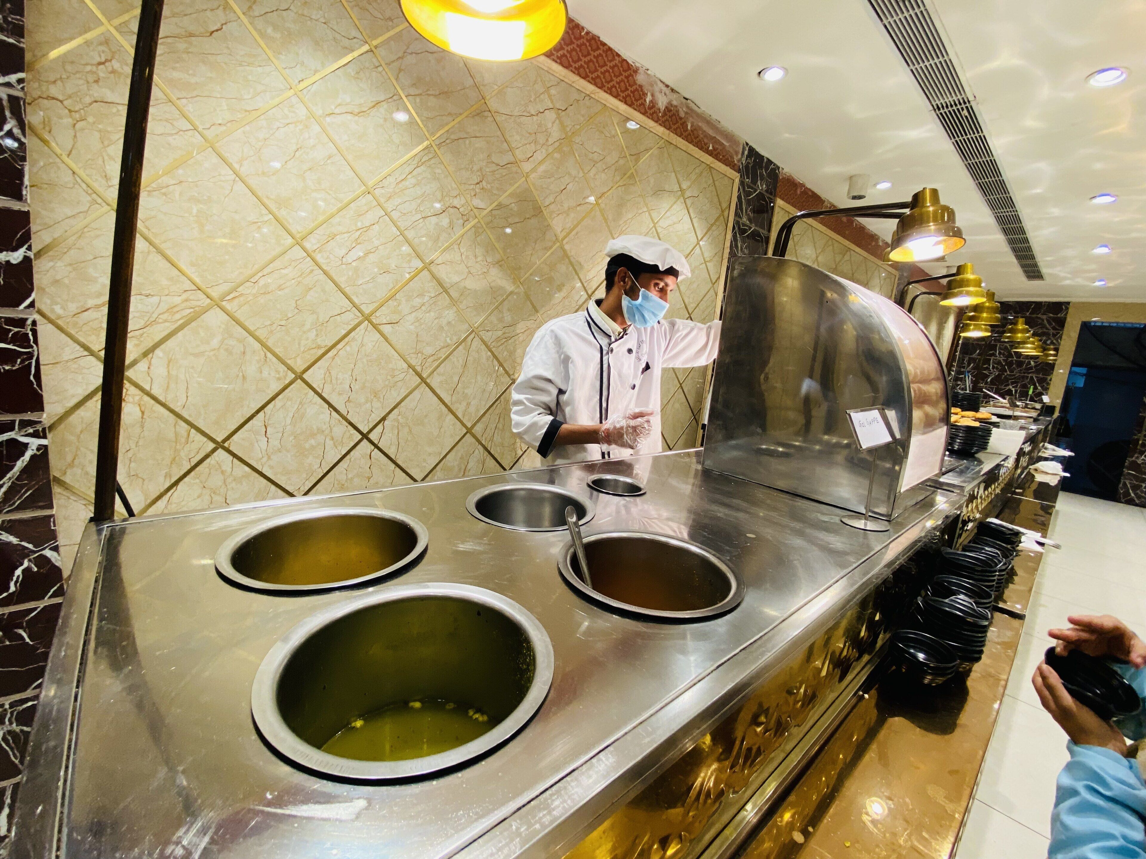 A buffet setup with multiple serving stations, a marble-tiled wall, and overhead lighting.