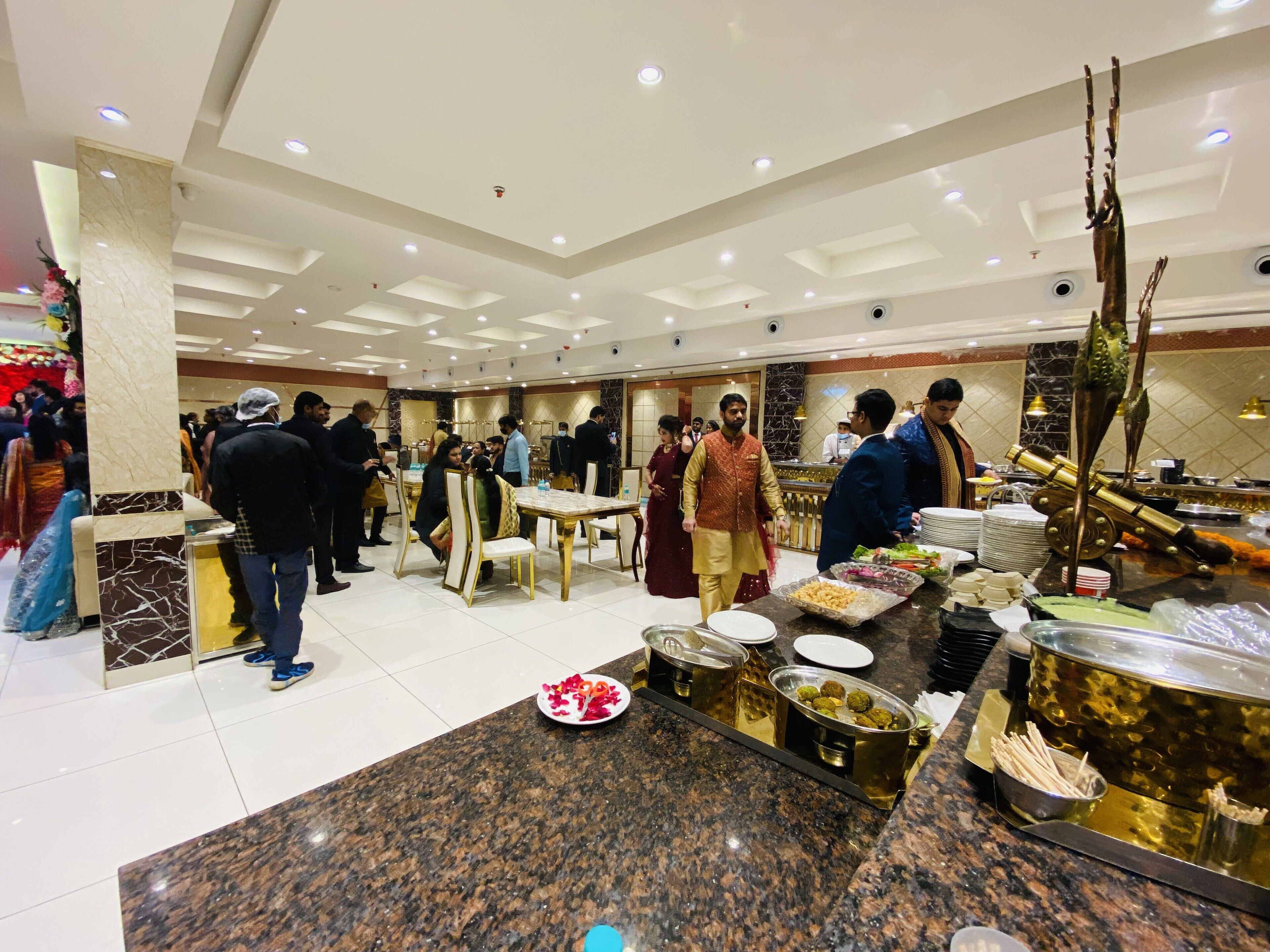 Un amplio salón de banquetes con suelo de mármol, varias mesas y una zona de buffet con diversas opciones de comida.