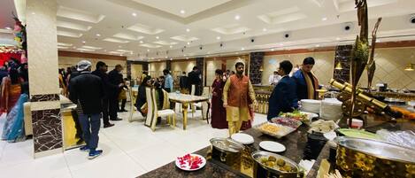 Un amplio salón de banquetes con suelo de mármol, varias mesas y una zona de buffet con diversas opciones de comida.