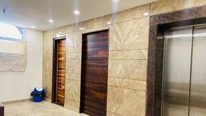 Un hall d’entrée avec un sol en marbre, des portes en bois et un ascenseur en verre.