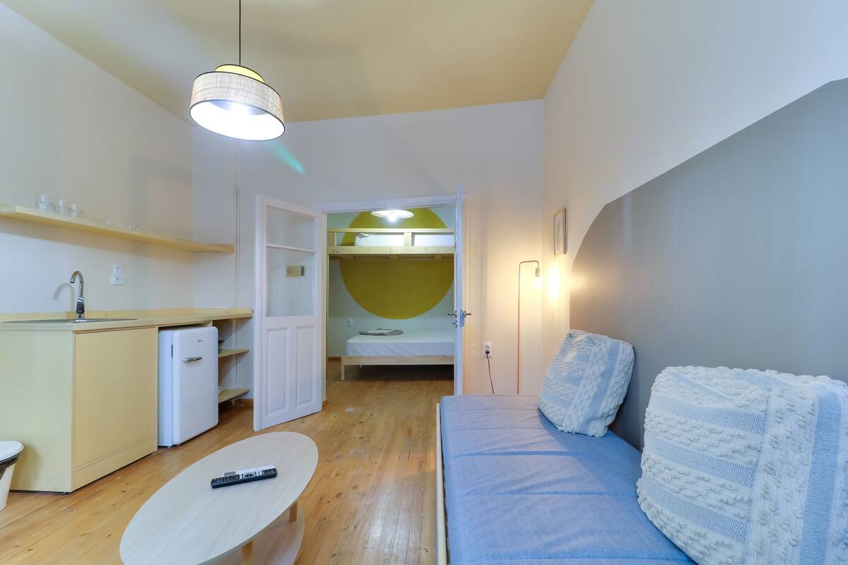A compact room with a kitchenette, a bed with a bunk, a sofa, and a small table.