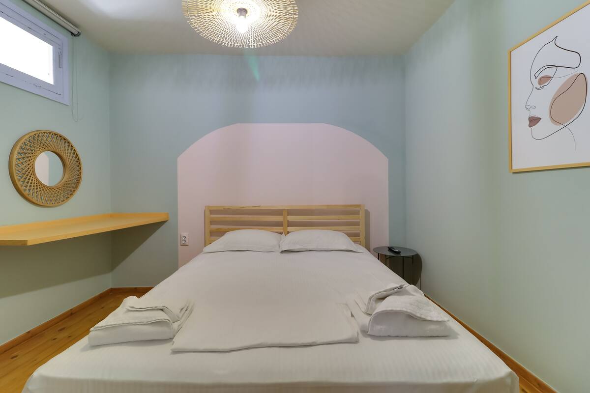 A neatly made bed with white linens, a wooden headboard, a bedside table with a lamp, and a wall-mounted mirror.